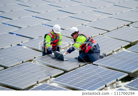 Two professional technician workers sit and work together using laptop in area of solar cell panel system in concept of green energy power plant. Two professional technician workers sit and work together using laptop in area of solar cell panel system in concept of green energy power plant. 111700294