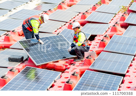 Two technician workers help to check and maintenance solar cell panels that set up over area of water reservoir. 111700388