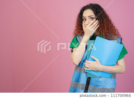 Front view of shocked, surprised woman with red, cturly hair standing, holding folders, closing mouth. Concept of aid. Front view of shocked, surprised woman with red, cturly hair standing, holding folders, closing mouth. Concept of aid. 111700968