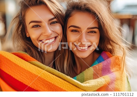 Joyful lesbian couple of two girls holding an LGBT flag in their hands, happiness and love concept 111701112