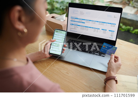 Woman entering information from credit card to pay for utility bills online Woman entering information from credit card to pay for utility bills online 111701599