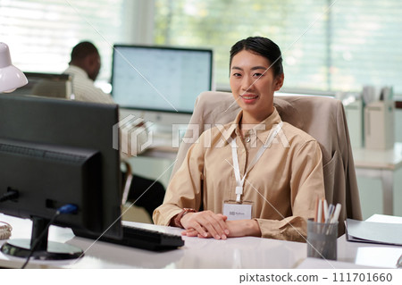 Portrait of smiling businesswoman checking text messages on smartphone when working at office desk 111701660