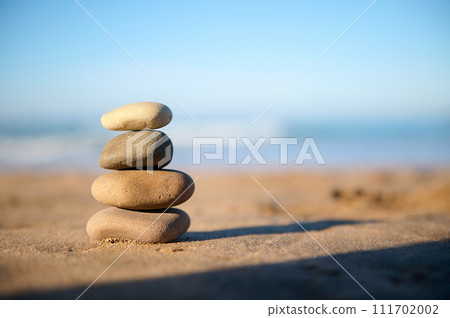 Still life with stacked pebbles, stones on the sandy beach against the background of Atlantic ocean with breaking waves Still life with stacked pebbles, stones on the sandy beach against the background of Atlantic ocean with breaking waves 111702002