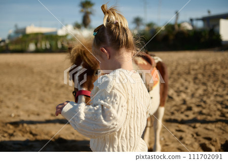 Rear view of a little child girl with a pony on the sandy beach Rear view of a little child girl with a pony on the sandy beach 111702091