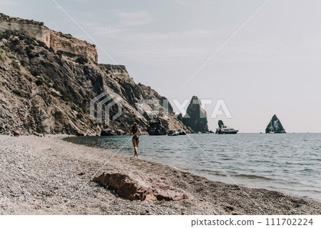 Woman beach vacation photo. A happy tourist in a blue bikini enjoying the scenic view of the sea and volcanic mountains while taking pictures to capture the memories of her travel adventure. 111702224