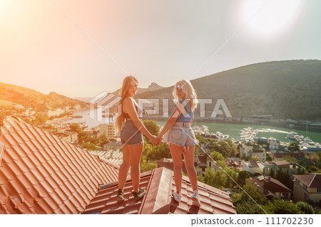 women standing on rooftop, enjoys town view and sea mountains. Peaceful rooftop relaxation. Below her, there is a town with several boats visible in the water. Rooftop vantage point. women standing on rooftop, enjoys town view and sea mountains. Peaceful rooftop relaxation. Below her, there is a town with several boats visible in the water. Rooftop vantage point. 111702230