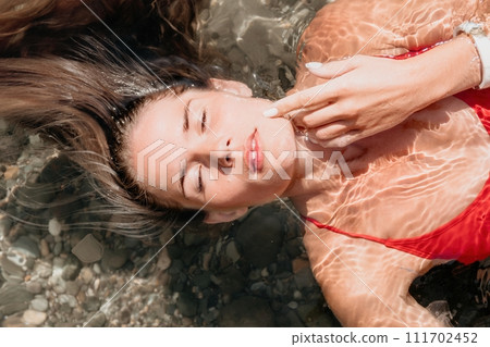 Woman travel portrait. close-up portrait of a happy woman with long hair in a red bikini, floating in water and smiling at the camera. Woman travel portrait. close-up portrait of a happy woman with long hair in a red bikini, floating in water and smiling at the camera. 111702452