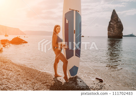 Woman sea sup. Close up portrait of happy young caucasian woman with long hair looking at camera and smiling. Cute woman portrait in bikini posing on sup board in the sea Woman sea sup. Close up portrait of happy young caucasian woman with long hair looking at camera and smiling. Cute woman portrait in bikini posing on sup board in the sea 111702483