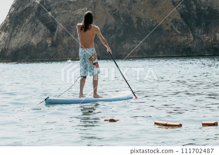 Man Sup Sea. Strong athletic man learns to paddle sup standing on board in open sea ocean on sunny day. Summer holiday vacation and travel concept. Aerial view. Slow motion Man Sup Sea. Strong athletic man learns to paddle sup standing on board in open sea ocean on sunny day. Summer holiday vacation and travel concept. Aerial view. Slow motion 111702487