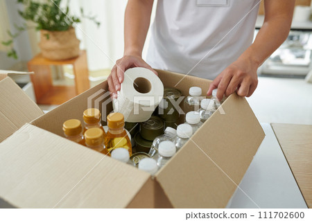 Volunteer putting food and necessities in cardboard box 111702600