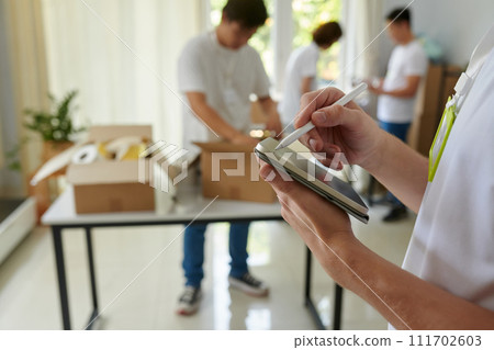 Manager of charity organization taking notes on tablet computer when volunteers packing boxes for refugees Manager of charity organization taking notes on tablet computer when volunteers packing boxes for refugees 111702603