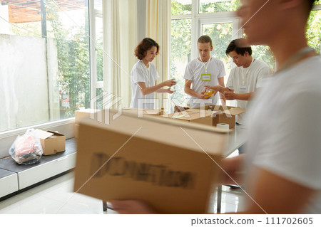 Diverse group of young people volunteering in charity organization, packing food in boxes Diverse group of young people volunteering in charity organization, packing food in boxes 111702605