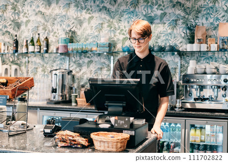 Young waiter serving customer at cash point in cafe. Man working with POS terminal. Cashier, barista checking for payment receipt. Hospitality, server and preparing a slip at the till in coffee shop 111702822