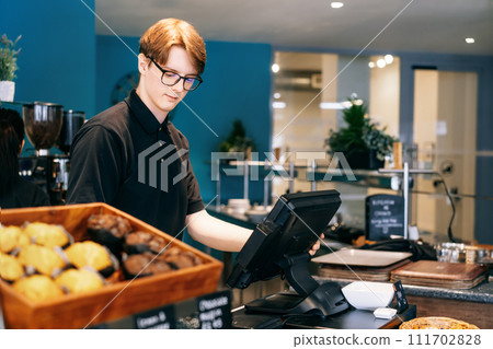 Young waiter serving customer at cash point in cafe. Man working with POS terminal. Student working part-time. Problems of unemployment and Job opportunities for youth. Small business vacancies 111702828