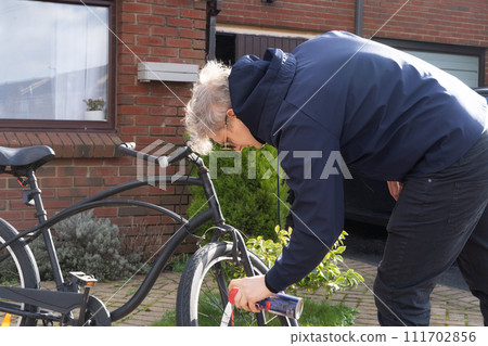 Young man in casual clothes cleaning rust and oiling his city cruiser bicycle chain and gear with spray before riding. Male doing DIY maintenance of his bicycle at home. Selective focus. Young man in casual clothes cleaning rust and oiling his city cruiser bicycle chain and gear with spray before riding. Male doing DIY maintenance of his bicycle at home. Selective focus. 111702856