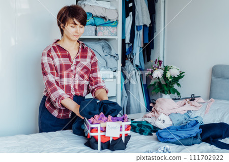 Woman selecting clothes from her wardrobe for donating to a Charity shop. Decluttering, Sorting clothes and Cleaning Up. Reuse, second-hand concept. Conscious consumer, sustainable lifestyle. Woman selecting clothes from her wardrobe for donating to a Charity shop. Decluttering, Sorting clothes and Cleaning Up. Reuse, second-hand concept. Conscious consumer, sustainable lifestyle. 111702922