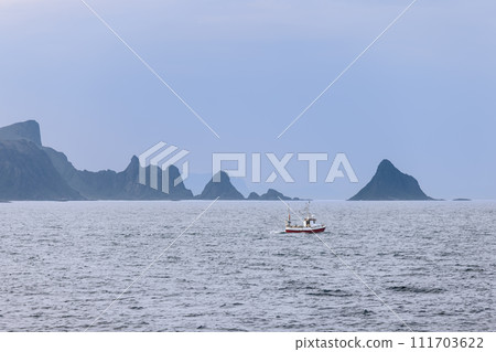 A solitary red fishing boat contrasts with the misty blues of the Norwegian Sea and Lofoten's peaks 111703622