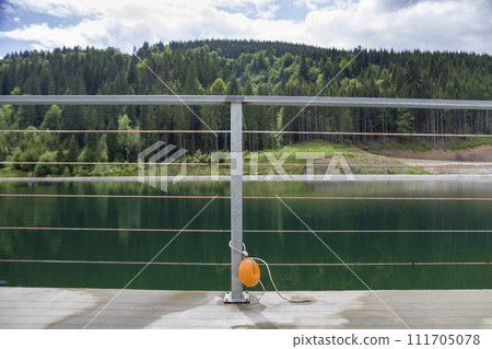 Yellow plastic buoy attached to a metal fence on the bank of a lake with green water. 111705078