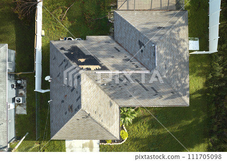 Wind damaged house roof with missing asphalt shingles after hurricane Ian in Florida. Repair of home rooftop concept 111705098