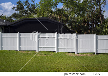 White vinyl picket fence on green lawn surrounding property grounds for backyard protection and privacy 111705116