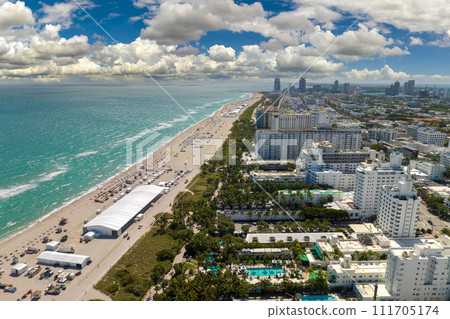Tourism infrastructure in southern USA. South Beach sandy surface with tourists relaxing on hot Florida sun. Miami Beach city with high luxury hotels and condos Tourism infrastructure in southern USA. South Beach sandy surface with tourists relaxing on hot Florida sun. Miami Beach city with high luxury hotels and condos 111705174