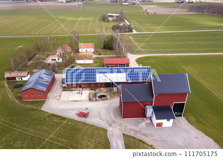 Top view of rural landscape on sunny spring day. Farm with solar photo voltaic panels system on wooden building, barn or house roof. Green field copy space background. Renewable energy production. Top view of rural landscape on sunny spring day. Farm with solar photo voltaic panels system on wooden building, barn or house roof. Green field copy space background. Renewable energy production. 111705175