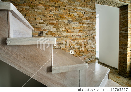 Stylish wooden contemporary staircase inside loft house interior. Modern hallway with decorative limestone brick walls and white oak stairs. Stylish wooden contemporary staircase inside loft house interior. Modern hallway with decorative limestone brick walls and white oak stairs. 111705217