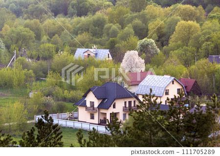 Quiet residential suburban area. Street with new modern comfortable brick cottages with yards and blooming gardens on background of beautiful green forest. Investments in real estate concept. 111705289