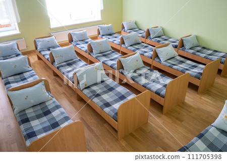 Many small beds with fresh linen in daycare preschool empty bedroom interior for comfortable afternoon nap of the kids. 111705398