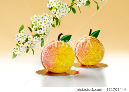 Sugared peach-shaped pastries on warm backdrop with blooming tree 111705444