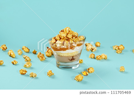 Caramel popcorn layered dessert in glass on blue background Caramel popcorn layered dessert in glass on blue background 111705469