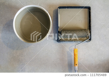 High angle of paint roller in tray with paint can on concrete floor. 111705489