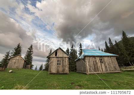 Old wooden shepherd huts on mountains green valley on blue cloudy sky copy space background. 111705672