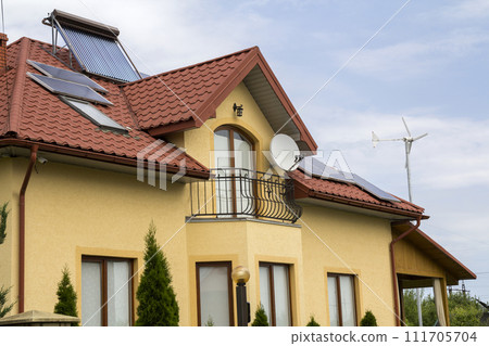 Close-up of new brick house top with red shingle roof, satellite dish, solar panels and plastic attic windows on bright blue sky background. Real estate property and professionally done work concept. 111705704