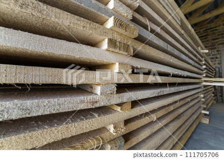 Neatly piled long stack of wooden boards inside attic room under construction. Neatly piled long stack of wooden boards inside attic room under construction. 111705706