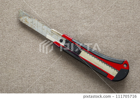 Close-up of isolated stationery retractable metallic knife with sharp blade on light cloth copy space background. Close-up of isolated stationery retractable metallic knife with sharp blade on light cloth copy space background. 111705716