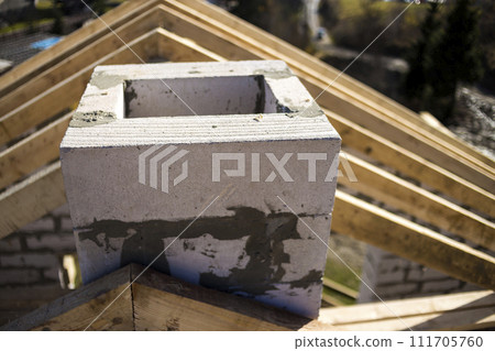 Close-up detail of roof frame of rough wooden lumber beams and chimney made of foam insulation blocks on blurred green background. Building, roofing, construction and renovation concept. 111705760