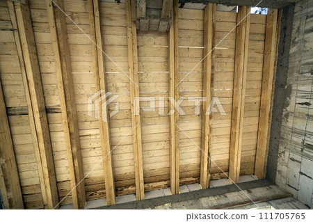 Close-up detail of house room interior under construction and renovation. Energy saving walls of hollow foam insulation blocks, wooden ceiling beams for roof frame. Close-up detail of house room interior under construction and renovation. Energy saving walls of hollow foam insulation blocks, wooden ceiling beams for roof frame. 111705765