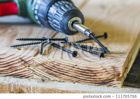 Close up of electric screwdriver with some screws laying on old rough wooden table or vintage natural planks. Building, repairing and home maintenance concept Close up of electric screwdriver with some screws laying on old rough wooden table or vintage natural planks. Building, repairing and home maintenance concept 111705788