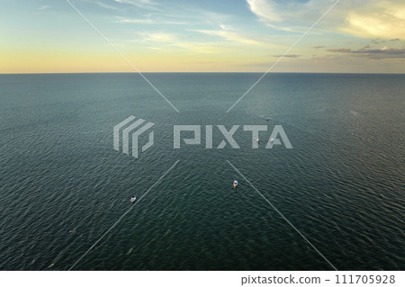 Aerial view of small yachts at sunset floating on sea waves with ripple surface. Motor boats recreation on ocean surface Aerial view of small yachts at sunset floating on sea waves with ripple surface. Motor boats recreation on ocean surface 111705928