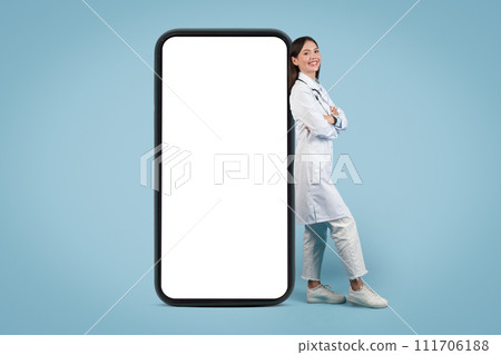 Young cheerful lady doctor leans on phone, arms crossed Young cheerful lady doctor leans on phone, arms crossed 111706188