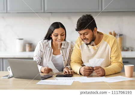 Smiling indian couple holding papers, calculating domestic bills, kitchen interior 111706193