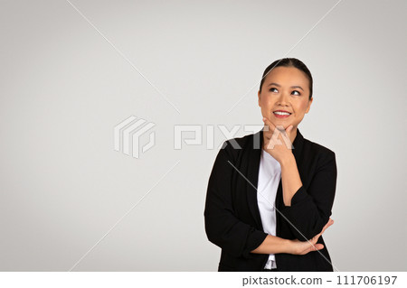 Contemplative Asian businesswoman with crossed arms looks upward, her finger on her chin Contemplative Asian businesswoman with crossed arms looks upward, her finger on her chin 111706197