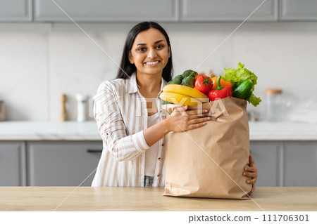 Cheerful young indian woman with paper bag full of grocery Cheerful young indian woman with paper bag full of grocery 111706301