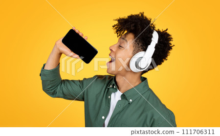 Joyful young black guy singing karaoke on yellow background 111706311