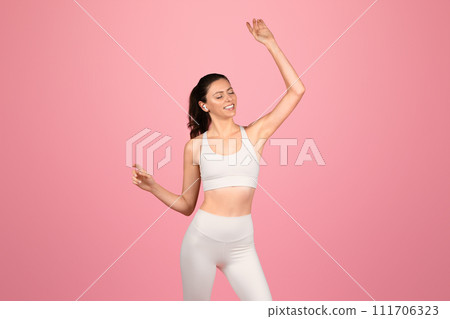 Vibrant young woman in sporty white attire joyfully dancing, with wireless earphones Vibrant young woman in sporty white attire joyfully dancing, with wireless earphones 111706323