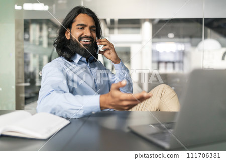 Indian Guy Talking On Cellphone Working On Computer At Office 111706381