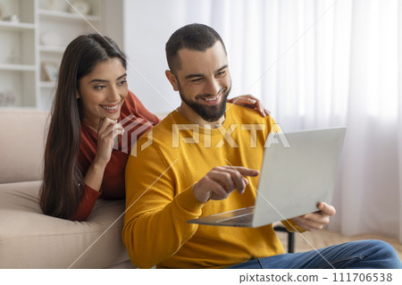 Happy young couple websurfing on laptop together while relaxing at home 111706538