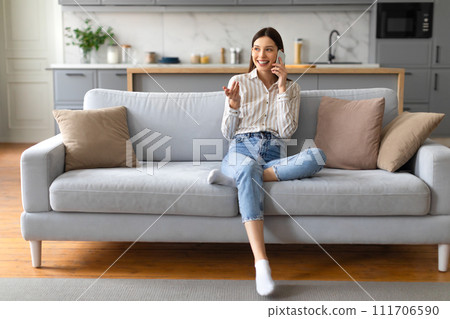 Cheerful young woman chatting on cellphone, sitting on sofa Cheerful young woman chatting on cellphone, sitting on sofa 111706590