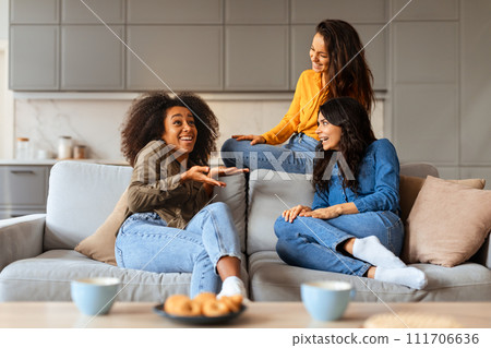 Multicultural trio of ladies chats joyfully around living room table Multicultural trio of ladies chats joyfully around living room table 111706636